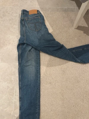 Blå jeansbyxor style REX 29/32 - Säljer ett par klassiska blå jeansbyxor i modellen REX, storlek 29/32. Jeansen har fem fickor, snygga kontrastsömmar och normal passform. Tillverkade i slitstarkt bomullsmaterial och perfekta till vardagslooken.
