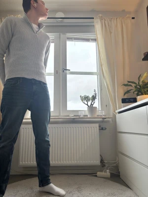 Ljusgrå ribbad half zip tröja - Säljer en stilren ljusgrå ribbad tröja med half zip och hög krage. Tröjan är långärmad och har en clean, modern look som passar perfekt till jeans. Materialet känns mjukt och är troligtvis bomull eller en bomullsblandning.