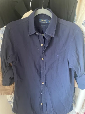 Marinblå skjorta Polo Ralph Lauren - Säljer en marinblå skjorta från Polo Ralph Lauren i slim fit. Skjortan har klassisk krage, långa ärmar och knappar framtill. Nästan aldrig använd och är i bra skick 