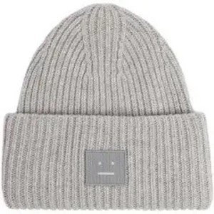 Grå ribbstickad mössa från Acne Studios - Grå ribbstickad mössa från Acne Studios med den ikoniska face-loggan framtill. Klassisk uppvikt kant och mjukt, värmande material som passar perfekt för kyliga dagar. Enkel och stilren design som funkar till alla outfits.