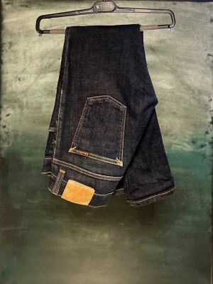 Nudie Jeans herr - Säljer ett par mörkblå slim fit jeans från Nudie Jeans med klassiska orange sömmar och femficksdesign. Jeansen har en snygg, smal passform och är tillverkade i slitstarkt jeansmaterial. Perfekta för dig som gillar stilrena och tidlösa jeans.
