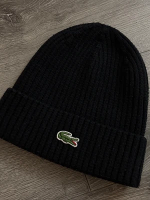 Mörk blå Lacoste mössa-Exklusiv - Stilren och tidlös mörkblå mössa från Lacoste med den ikoniska broderade krokodilloggan framtill. Ribbstickad design som ger en skön passform och håller formen bra. Lätt att matcha till både vardags- och streetwear-outfits.  • Färg: Mörkblå • Original Lacoste • Klassisk krokodillogga • Ribbstickad & bekväm • Unisex • Bra skick  Perfekt för höst och vinter – enkel, clean och alltid rätt.