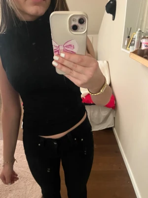 Svart ärmlös polotopp - Säljer en svart, tight polotopp utan ärmar. Toppen har hög krage och är croppad i modellen, vilket ger en clean och stilren look. Perfekt att matcha med jeans eller kjol för en enkel men snygg outfit.