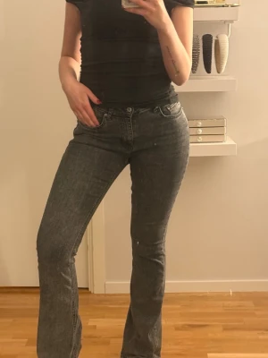 Grå bootcut jeans från Perfect Jeans - Säljer ett par grå bootcut jeans från Perfect Jeans i storlek 38. Jeansen har klassisk femficksdesign, dragkedja och knapp framtill samt en snygg tvättad look. Materialet är mjukt jeans-tyg som sitter skönt och följer kroppen. Skavanker längst ner vid benen. 