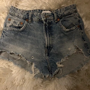Blåa jeansshorts från Zara - Blåa  jeansshorts från Zara i denim med slitna kanter. Jättebra skick! Midjemått: 30cm