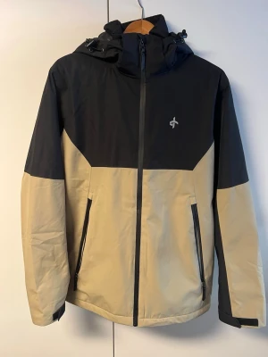 Beige och svart skidjacka - Säljer en beige och svart skidjacka från Cross Sportswear i storlek S. Jackan har huva med snörning, hel dragkedja framtill och två fickor med dragkedja. De två framfickor är stora och har plats med mycket. Jackan har även en armficka som sitter vänster arm där du kan ha ditt liftkort eller mobil i. Även på sista bilden ser du ett fack som inte har dragkedja. Om du har några frågor så svarar jag snabbt! Frakt sker inom 24 timmar!📦💨 OBS! priset kan diskuteras.