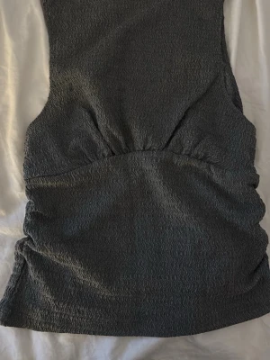 Grå ribbad linne Pull&Bear - Säljer en grå ärmlös topp från Pull&Bear i storlek S. Tyget har en ribbad struktur med vågigt mönster som ger en cool look. Modellen är figurnära och stretchig, perfekt till jeans eller kjol.
