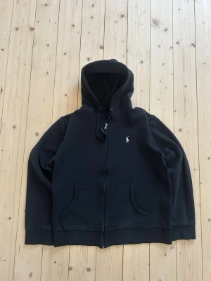 Svart Ralph Lauren Zip Hoodie - Klassisk Ralph Lauren hoodie i svart färg. Tröjan är i mycket bra skick. | Sparsamt använd |  Storlek: M | Skick: Mycket bra skick! | Färg: Svart | Märke: Ralph Lauren | Modell: Hoodie med dragkedja |  Hör gärna av dig vid frågor så svarar jag så fort jag kan! 😁| 