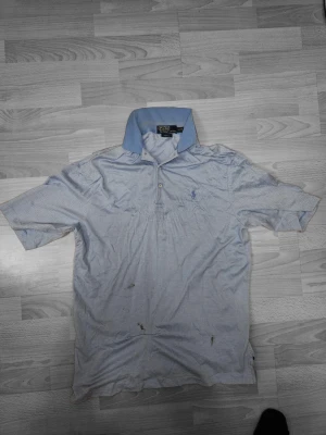 Blå mönstrad Polo Ralph Lauren skjorta - Säljer en blå kortärmad skjorta från Polo Ralph Lauren i modellen Golf Fit. Skjortan har ett diskret fiskbensmönster, klassisk krage och har den ikoniska broderade loggan på bröstet.