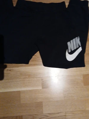 Nike byxor - Svarta mjukisbyxor från Nike med stor vit logga på ena benet. Sköna och avslappnade, perfekta för chill eller träning. Tillverkade i mjukt material som känns bekvämt mot huden.