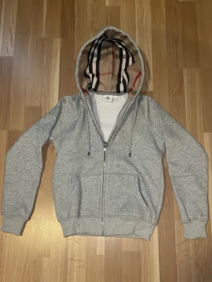Burberry hoodie - Säljer en skön burberry hoodie i grå färg, hoodien saknar logga men är ändå väldigt stiligt och passar till nästan allt! Den är i nytt skick, den är oanvänd. Den känns som XS