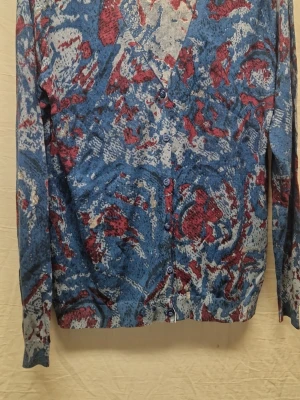 Mönstrad kofta från Tiger of Sweden - Unik kofta från Tiger of Sweden i blått, vinrött och grått abstrakt mönster. Långärmad med knappar framtill och V-ringning. Stickad i mjukt material, perfekt för dig som vill sticka ut med en cool och färgstark look.