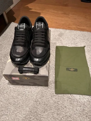 Valentino Rockrunner sneakers svart camo - Säljer ett par Valentino Rockrunner  i svart med camo-mönster. Skorna har en mix av mocka och skinn, samt coola nitar på hälen. Klassisk snörning och chunky sula för extra attityd. Kommer med originalkartong och dustbag snören.