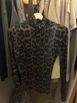 Leopardmönstrad polotopp från Amisu - Säljer en leopardmönstrad polotopp från Amisu i bruna och svarta toner. Toppen har lång ärm och en hög krage som ger en snygg siluett. Materialet är mjukt och stretchigt, perfekt för att styla med jeans eller kjol.