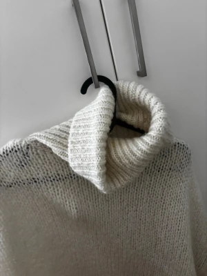 Vit stickad polotröja - Mysig vit stickad polotröja med oversized passform och bred, ribbad polokrage. Perfekt för kalla dagar och enkel att styla med jeans eller kjol. Tröjan har långa ärmar och är riktigt fluffig och skön.