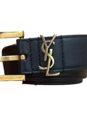 Svart skinnbälte från Yves Saint Laurent - Säljer ett svart bälte i äkta skinn från Yves Saint Laurent med ikoniskt YSL-emblem i guld och matchande guldfärgat spänne. Perfekt accessoar för att lyfta vilken outfit som helst med en lyxig touch.