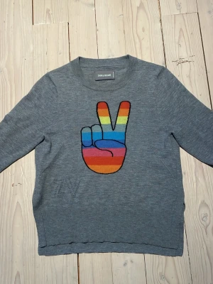 Grå stickad cashmere tröja Zadig & Voltaire - Säljer en grå stickad tröja från Zadig & Voltaire med ett stort regnbågsfärgat peace-tecken på bröstet. Tröjan har rund hals, långa ärmar och diskret ZV-detalj på sidan. Perfekt för dig som vill ha en färgklick i garderoben. Tröjan är 100% cashmere! Den är använde fåtalgånger.