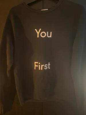 Svart sweatshirt Acne Studios M - Svart sweatshirt från Acne Studios i storlek M med vit text 'You First' på framsidan. Tillverkad i 100% bomull, har rund halsringning och långa ärmar. Perfekt för en clean och avslappnad stil.