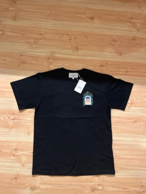 Svart t-shirt från Casablanca - Svart t-shirt från Casablanca med färgglad tryckt grafik fram och stort tryck på ryggen med texten 'Avenida Casablanca' och ett fönster med byggnadsmotiv. Klassisk passform och rund hals. Tillverkad i mjuk bomull för skön känsla.