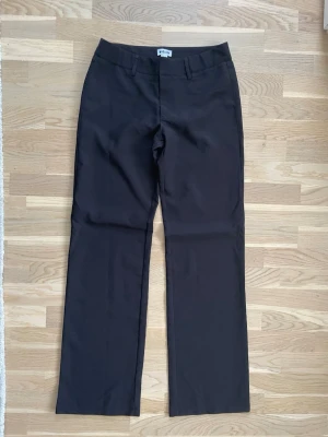 Svarta kostymbyxor från Madlady, tall low - Svarta kostymbyxor från Madlady i rak modell. Byxorna har hällor för bälte, två fuskfickor bak och klassisk midja. Materialet känns oklart men är slätt och har en dressad look. Perfekta till en clean och stilren outfit. Använt par gånger helt som nya