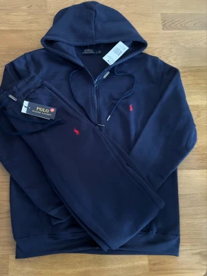 Polo Ralph Lauren mjukisset / tracksuit – Hoodie & byxor – Marinblå – Ny med tags - Säljer ett original Polo Ralph Lauren mjukisset / tracksuit i marinblå färg, bestående av zip-hoodie med huva och matchande mjukisbyxor.  ✨ Helt nytt med tags kvar – aldrig använt. ✨ Klassisk och tidlös design med broderad Polo-logga. ✨ Perfekt passform och hög kvalitet, precis som man förväntar sig av Ralph Lauren. ✨ Passar både vardag, resor och avslappnad stil.  Setet är svårt att få tag på och väldigt eftertraktat. Snabb affär prioriteras – öppen för seriösa prisförslag.  📦 Skickas snabbt 