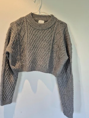 Croppad stickad tröja H&M - Stickad tröja i kort modell från H&M med flätstickat mönster i en kall grågrön nyans.