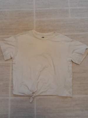 Vit knyt t-shirt - Enkel vit t-shirt från H&M Basic i ekologisk bomull. Modellen har korta ärmar och en snygg knytning längst ner framtill som ger en avslappnad vibe. Perfekt till jeans eller shorts för en chill look. !!endast swish +frakt!!