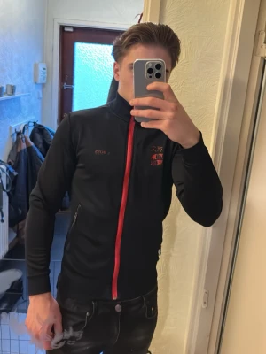 Hugo boss SÄLLSYNT zip tröja  - Köpt på bestsecret!! Helt okej skick då Hugo boss trycket där fram saknar 2 bokstäver. Den säljs i samma skick som på bilderna.                    Svart långärmad ziptröja från BOSS med röd dragkedja och röda japanska tecken på bröstet och ryggen. Tight passform och hög krage. Snygga broderade detaljer och fickor med dragkedja. Perfekt för dig som gillar streetwear med unik touch.