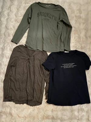 3-pack t-shirts från Reaction, Vero Moda & CRW - Säljer tre t-shirts: en grön långärmad från Reaction med Brooklyn-tryck, en brunmelerad långärmad från Vero Moda Denim med snörning fram och en mörkblå kortärmad från CRW med vit text framtill. Alla i mjuk bomull och perfekta till vardags.