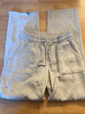 Grå mjukisbyxor från 157, storlek S - Mysiga ljusgrå mjukisbyxor från 157 med resår och snörning i midjan. Byxorna har stora fickor fram och bak, raka ben och är gjorda i mjukt bomullsmaterial med fleece på insidan. Perfekta för chill dagar eller när du vill vara extra bekväm. Obs har en fläck vid slutet av benet som man kan se på bilden!