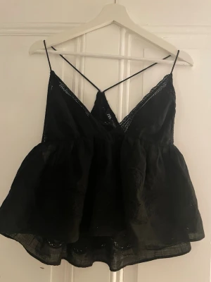 Svart linnetopp från Zara med spets - Supersöt svart linnetopp från Zara med tunna axelband. Toppen har v-ringning och fina spetsdetaljer längs kanterna samt broderade mönster i tyget. Perfekt för varma dagar eller att styla lager på lager.
