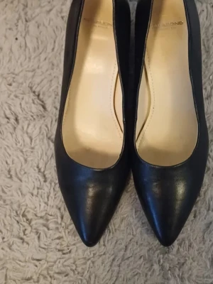 Svarta pumps från Vagabond - Klassiska svarta pumps från Vagabond med spetsig tå och låg klack. Skorna är tillverkade i skinn och har en stilren design som passar till många olika outfits. Perfekta för dig som gillar en tidlös och elegant look.