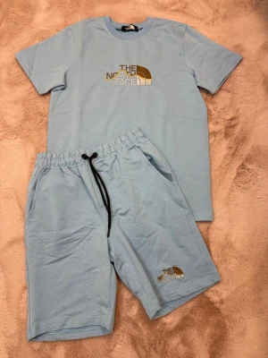 The North Face - Bilderna visar ett ljusblått set med t-shirt och shorts från The North Face, båda i mjuk bomull och med broderad logga framtill.