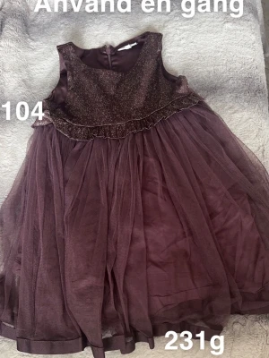 Glittrig lila tyllklänning barn - Supersöt lila klänning med glittrigt liv och volangdetalj upptill. Kjolen är i flera lager tyll som ger en fluffig känsla. Perfekt för speciella tillfällen och har en klassisk rund halsringning samt dragkedja bak.🌸 Använd en gång. Storlek 104