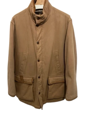 Beige parkajacka från Loro Piana - Säljer en beige parkajacka från Loro Piana med klassisk design. Jackan har hög krage, knäppning med knappar och flera stora fickor framtill.  Skriv vid intresse och vid behov av fler bilder! 