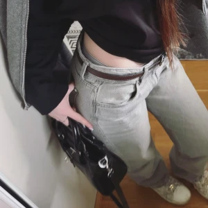 Gråa wide jeans - Säljer ett par gråa jeans med wide fit och låg midja. Byxorna har klassisk femficksdesign och kommer med ett brunt bälte. Perfekta för en avslappnad och trendig look.