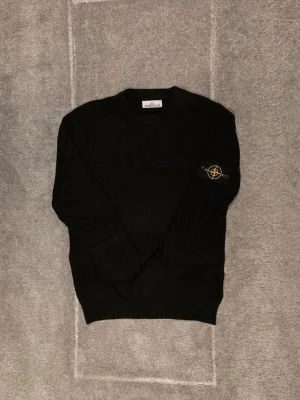 Svart stickad tröja från Stone Island - Säljer en svart stickad tröja från Stone Island med klassisk märke på ärmen. Tröjan är som ny och har bara använts ett fåtal gånger eftersom jag växte ut den för snabbt. Qr koden funkar såklart. Har också kvar tagsen. Priset är ej hugget i sten. Äkta!