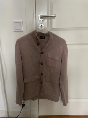 Beige stickad kofta från Sand - Säljer en beige stickad kofta från Sand Copenhagen. Koftan har ribbad krage, stora knappar framtill och tre fickor med lock. Storlek: M. Skick: 8/10. Vi köp av flera produkter från min sida erbjuds ett lägre pris!