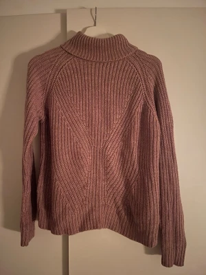 Rosa polotröja från Jacqueline de Yong - Mysig rosa polotröja från Jacqueline de Yong i storlek S. Tröjan är stickad med ett snyggt ribbat mönster och har lång ärm samt hög polokrage. Perfekt för kyliga dagar och enkel att styla med jeans eller kjol.