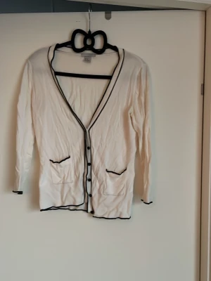 Vit kofta med svarta detaljer - Säljer en vit kofta från hm med svarta kanter och knappar. Koftan har två fickor framtill och lång ärm. Tunn och mjuk i materialet, perfekt för lager på lager. Enkel och stilren design som passar till det mesta❤️❤️En riktig favorit 