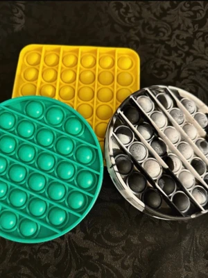 Tre pop it fidget-leksaker - Säljer tre pop it fidget-leksaker i olika färger och former. En rund i svartvitt mönster, en rund i turkos och en fyrkantig i gul. Perfekta för att hålla händerna sysselsatta och stressa ner. Alla är gjorda i mjuk silikon.