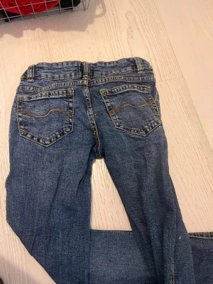 Blå bootcut lågmidjade jeans  - Ett par klassiska blå jeans från 157 med bootcut passform. Jeansen har kontrastsömmar i gult, fem fickor och bälteshällor. Materialet är slitstarkt jeans-tyg i bomull och de har en tidlös look som funkar till allt.