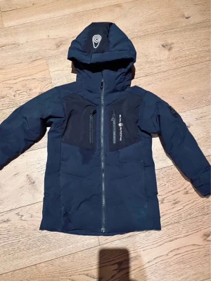 Mörkblå Sail Antarctica vinterjacka - Säljer en mörkblå vinterjacka från Sail Antarctica med huva och snygga detaljer. Jackan har två bröstfickor med dragkedja, patch på ärmen och logga på huvan. Perfekt för kalla dagar och riktigt skön passform.