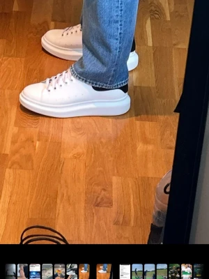 Vita Alexander McQueen sneakers - Säljer ett par feta vita sneakers från Alexander McQueen med svart detalj på hälen och chunky plattformssula. Skorna har klassisk snörning och är tillverkade i skinn, perfekta för dig som vill sticka ut med stilrena men ändå unika sneakers.