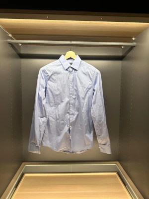 Ljusblå skjorta Tiger of Sweden - Klassisk ljusblå skjorta från Tiger of Sweden i slim fit-modell. Skjortan har långa ärmar, knappar framtill och en stilren krage. Tillverkad i mjuk bomull som känns skön mot huden. Perfekt för dig som gillar en clean och enkel look.