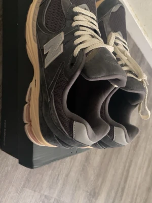 New Balance grå sneakers 2002r mocka mesh - Säljer ett par New Balance sneakers i mörkgrå mocka och mesh med beige sula och vita snören. Skorna har den klassiska N-loggan på sidan och en robust, mönstrad yttersula för bra grepp. Perfekta för dig som gillar stilrena och bekväma sneakers. Helt nya och oanvända. Pris är kan diskuteras vid snabb affär.