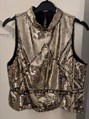 Glittrig guld topp med paljetter - Säljer en galet snygg topp i guldpaljetter och geometriska detaljer. Perfekt för att sticka ut och få all eyes on you på nyår. Har bara använts en gång. Allt är i mycket bra skick 