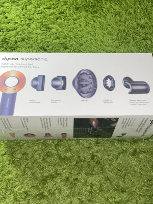 Dyson Supersonic hårfön med tillbehör - Dyson Supersonic hårfön i silver och koppar med flera stylingmunstycken: stylingkoncentrator, smoothing nozzle, diffuser, gentle air och flyaway attachment. Innovativ design med digital motor och avancerad värmekontroll. Perfekt för att skapa olika hårlooks.