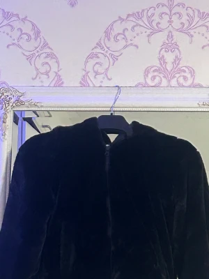 Svart pälsjacka med dragkedja - Mjuk och fluffig svart pälsjacka med dragkedja framtill. Jackan har ribbade muddar med silvriga detaljer vid ärmslut och nederkant. Perfekt för dig som gillar en chill och snygg look med lite extra edge.