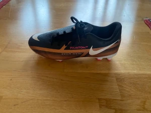 Nike Phantom GT fotbollsskor svart/koppar - Säljer ett par Nike Phantom GT fotbollsskor i svart med kopparfärgade och rosa detaljer. Skorna har snörning, vit sula med rosa dobbar och en snygg, sportig design. Ovandelen är i syntetmaterial för bästa bollkontroll och passform. Perfekta för dig som vill sticka ut på planen.  Har endast använts enstaka gånger.